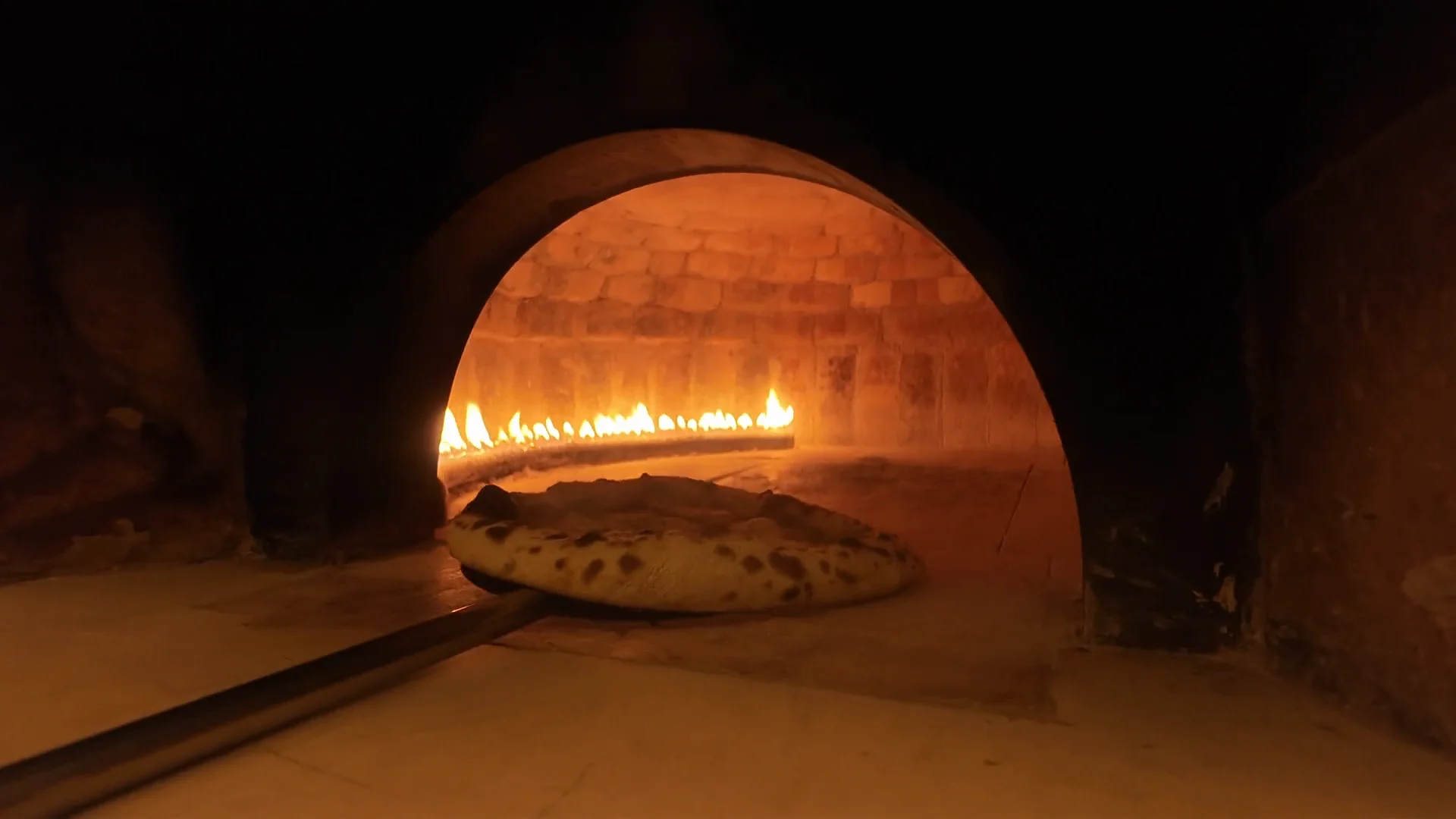 La pizza che entra nel forno a legna sulla pala, con le fiamme in fondo