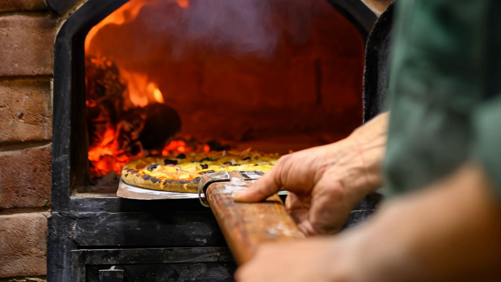 La pizza che entra nel forno a legna sulla pala, con le fiamme