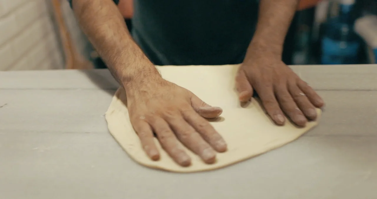 Due mani che stendono l’impasto della pizza sul banco infarinato